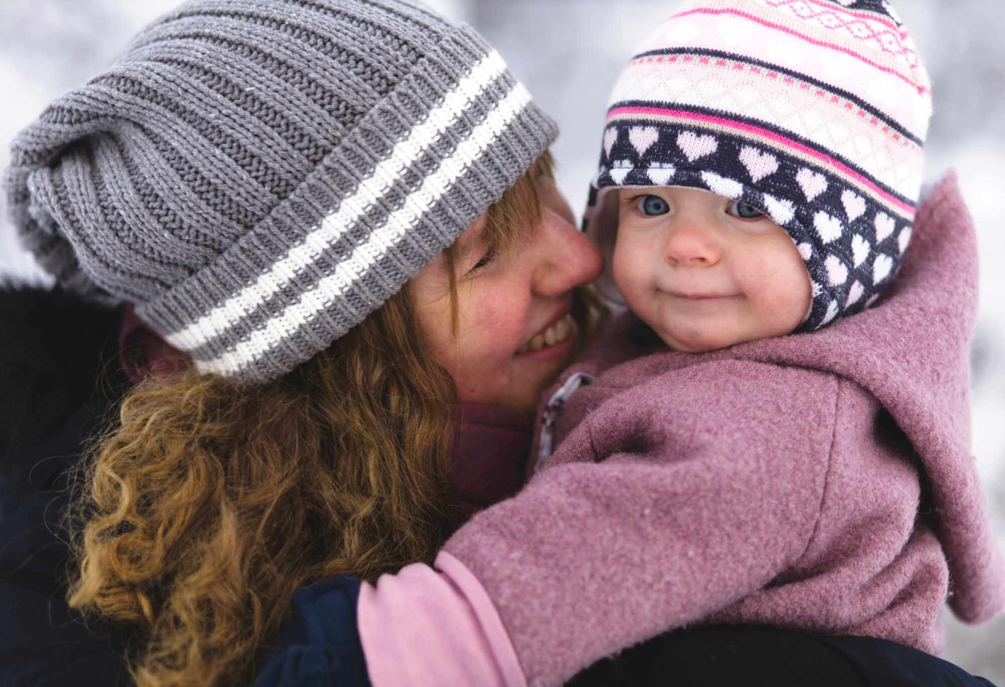 Mutter lacht kleines Kind auf dem Arm an in Winterkleidung